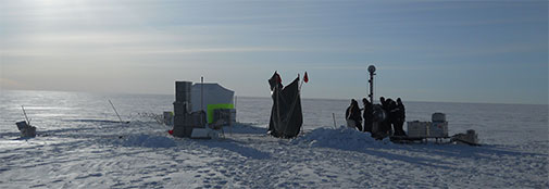 The shallow drilling operation takes place a little away from main camp to get away from the exhaust from the generators and other pollutants. From left to right the tent with firn gas pumping equipment (partially hidden behind a stack of ice core boxes), a tarp used to provide shade, and the shallow drill.