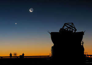 I forgrunden ses VLT (Very Large Telescope) og i baggrunden til venstre ses halvmåne og planeten Venus. Credit: ESO